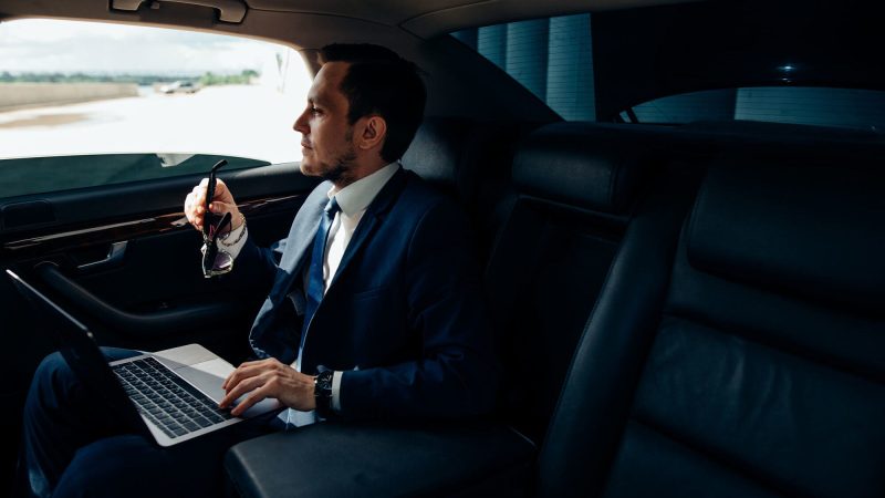 executive in chauffeured car using laptop for business travel